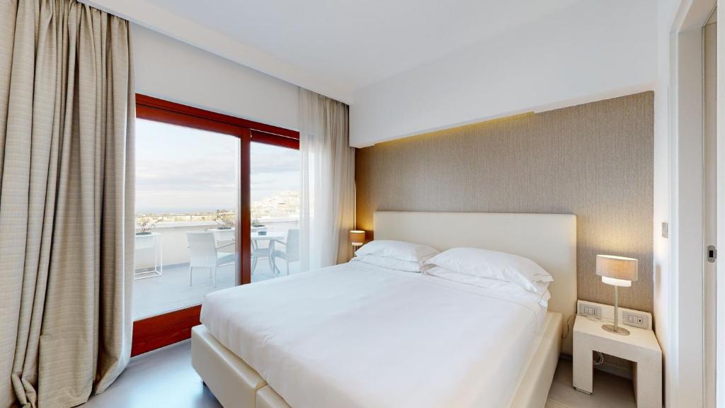 a bedroom with a white bed and a balcony at Hotel Monte Sarago in Ostuni