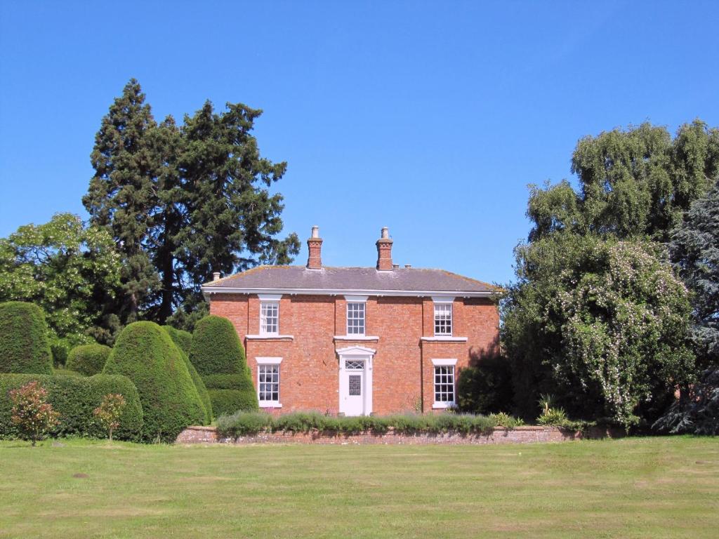 ein großes rotes Backsteinhaus mit Bäumen und Sträuchern in der Unterkunft The Grange in East Barkwith