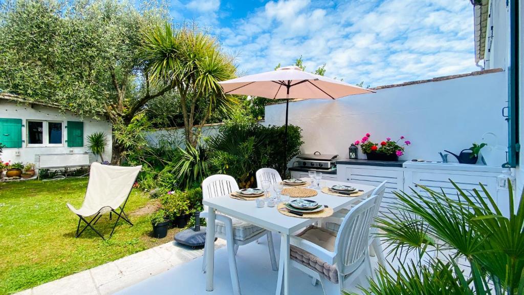 - une table blanche avec des chaises et un parasol sur la terrasse dans l'établissement jolie maison de vacances a proximitée du port et des commerces et de la plage, à La Flotte