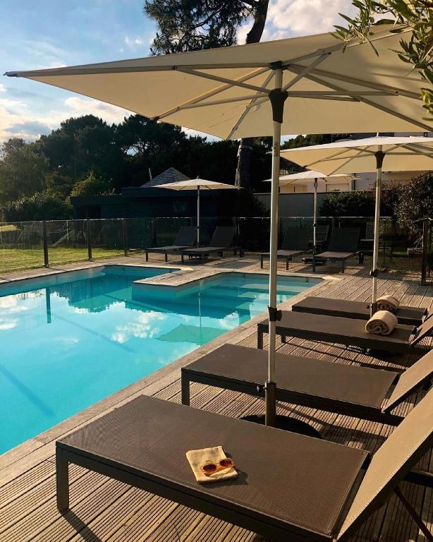 - une piscine avec 2 chaises longues et un parasol dans l'établissement Villa Mané Lann Maison d'hôtes & spa, à Carnac