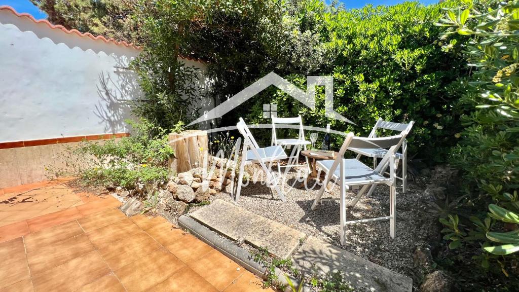 two white chairs and a table in a garden at MiRADOR DEL FARO in Cala en Bosc