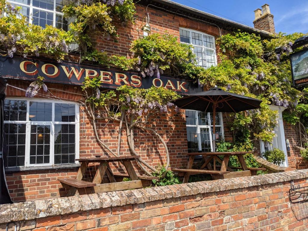 a brick building with two tables and an umbrella at Cowpers Oak in Olney