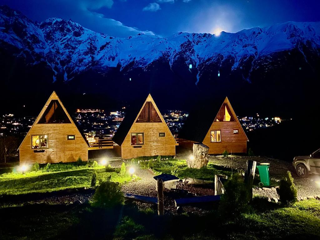 a group of wooden cabins with mountains in the background at Little Wood House Gergeti in Stepantsminda