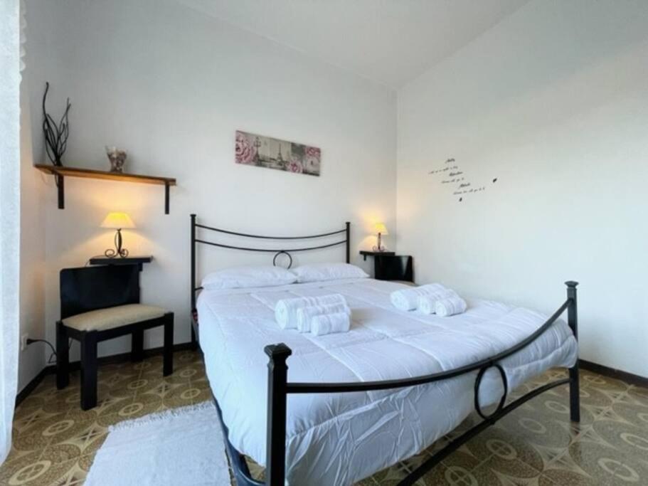 una camera da letto con un letto con lenzuola bianche e una sedia di [Loano 2] parcheggio privato - wifi- giardino a Loano