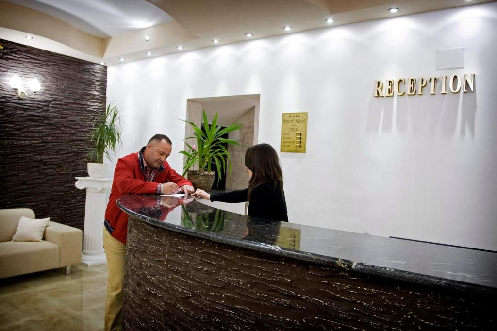 mężczyzna i kobieta stojący przy recepcji w obiekcie RHC Royal Hotel w mieście Oradea