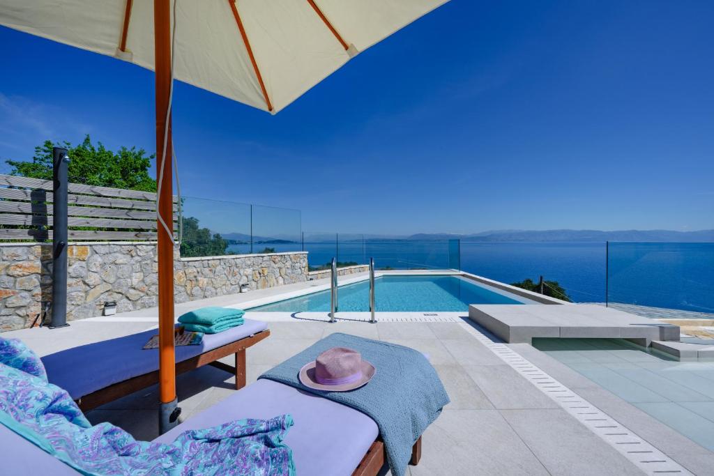 a villa with a swimming pool and an umbrella at Sea & Cliff Luxury Suites in Benitses