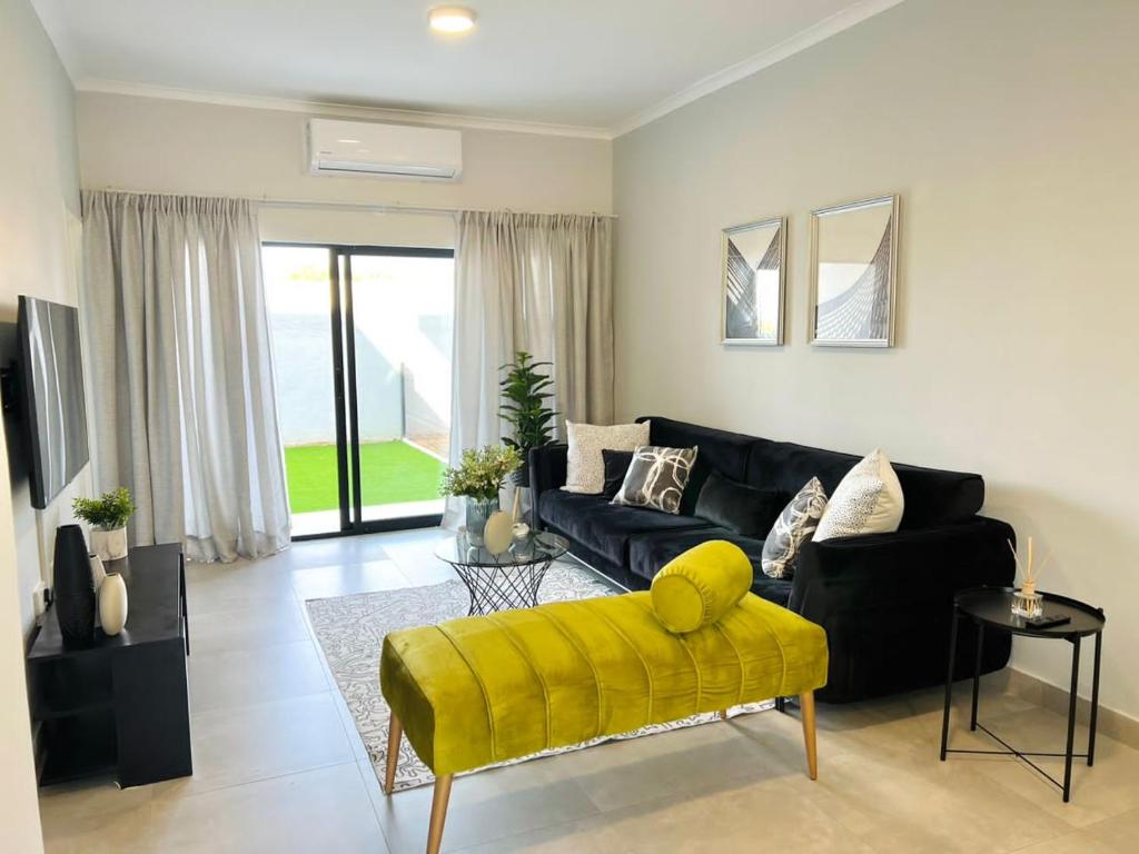 a living room with a black couch and a yellow chair at E105 Sarona City Flat E105 in Gaborone