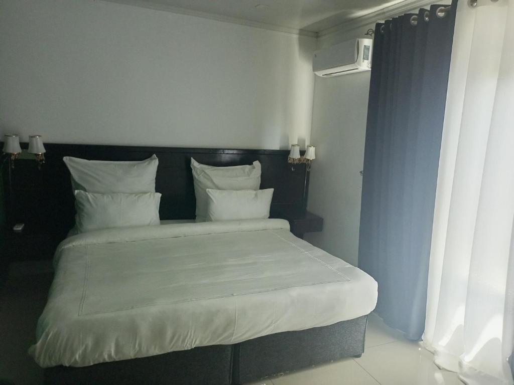 uma cama com lençóis brancos e almofadas num quarto em The Furnished Apartments em Livingstone