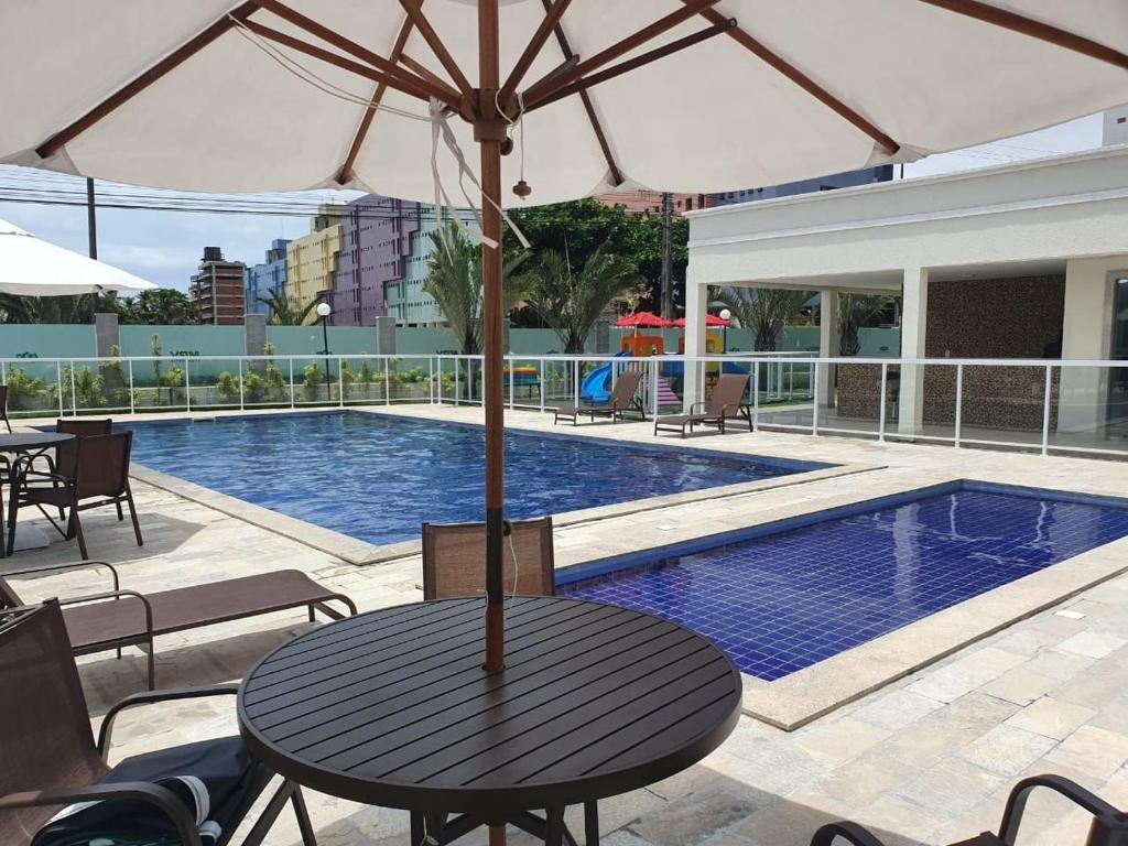 a table with an umbrella next to a swimming pool at Spazio Jardins do Litoral in Cabedelo