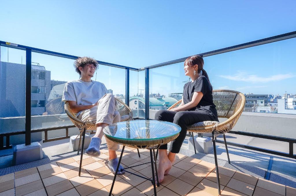 Ein Mann und eine Frau, die auf einem Balkon auf Stühlen sitzen in der Unterkunft unito KEIKYU-KAMATA in Tokio