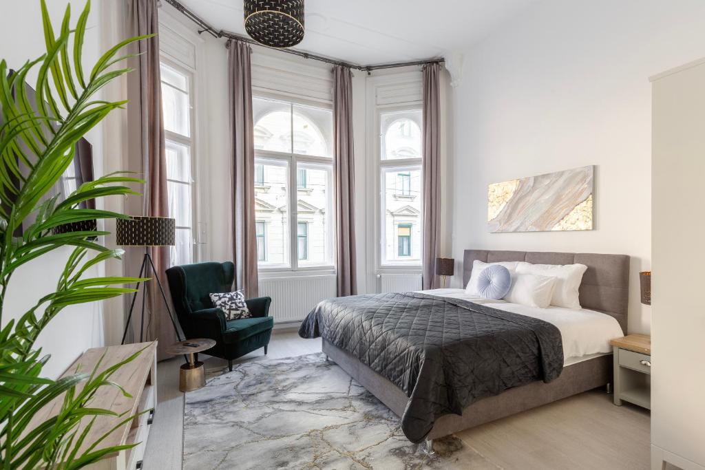 a bedroom with a bed and a chair and windows at LH Gallery Apartments in Budapest