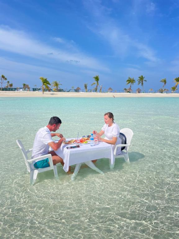 Ein Mann und eine Frau sitzen an einem Tisch am Strand in der Unterkunft Seginy Seaview in Guraidhoo