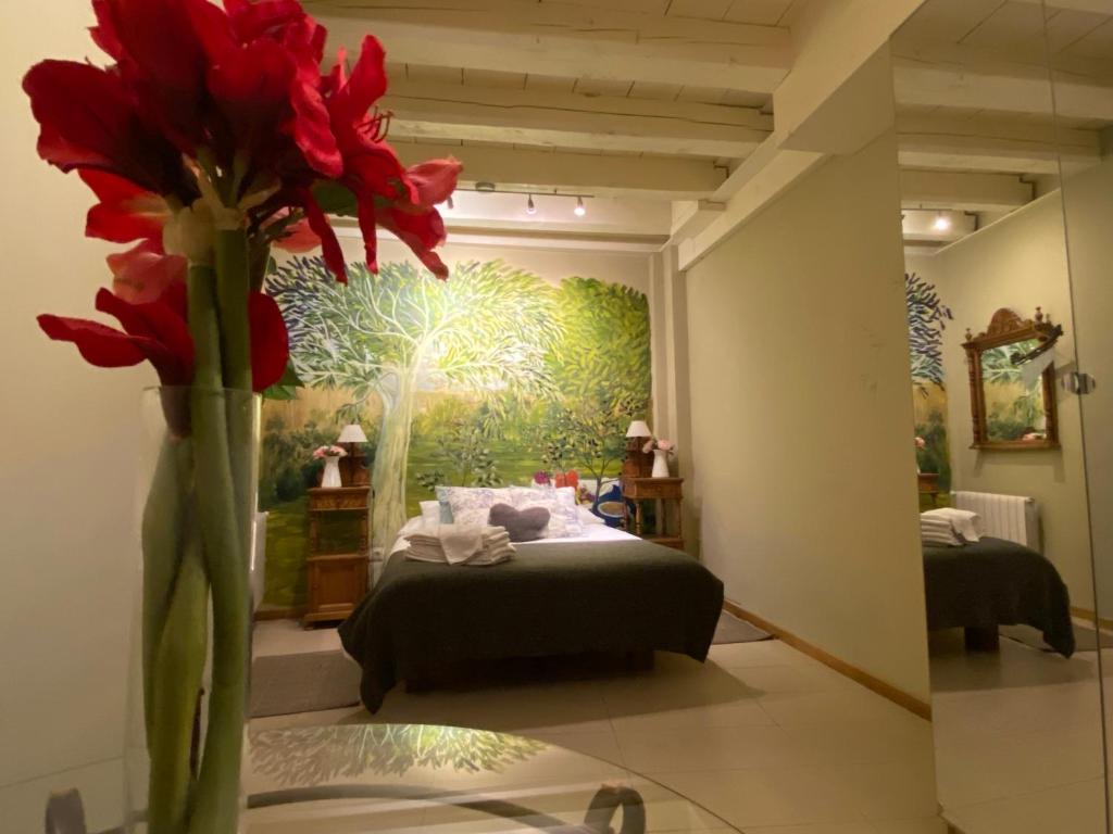 Cette chambre comprend un lit et un vase avec des fleurs rouges. dans l'établissement Refitolería Apartamentos, à Ségovie