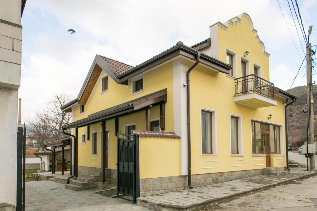 uma casa amarela com uma porta preta numa rua em Къща за гости КООП Флорал / COOP Floral Guest House 