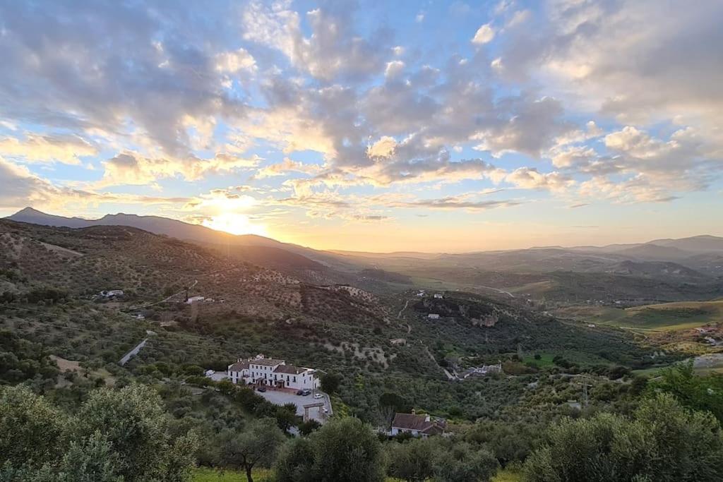 einen Sonnenuntergang über einem Tal mit einem Haus auf einem Hügel in der Unterkunft Entre Vistas in Zahara de la Sierra