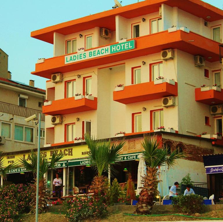 Ladies Beach Hotel في كوساداسي: مبنى فيه فندق شاطئي فيه نخل امامه