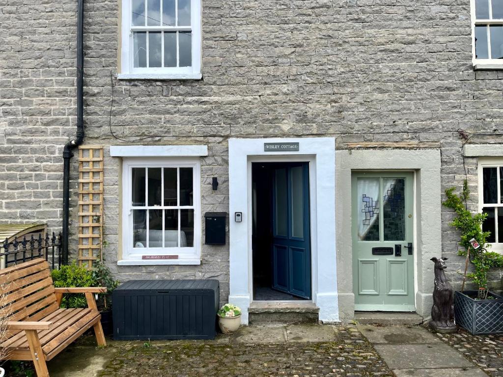 una casa de ladrillo con una puerta azul y un banco en Wesley Cottage, en Middleham