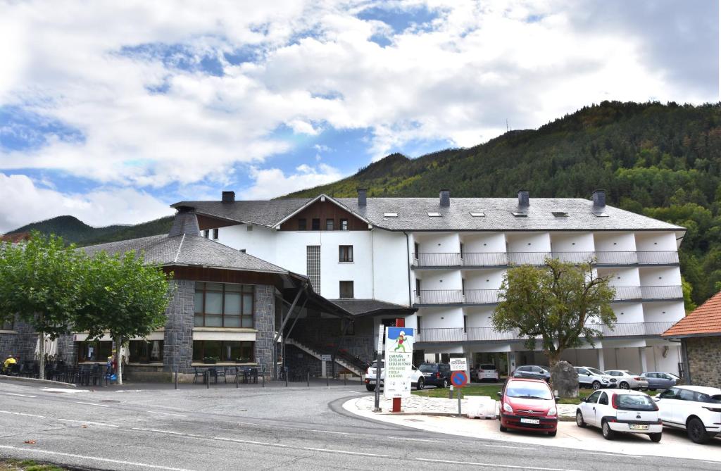 un gran edificio blanco con coches aparcados en un aparcamiento en Hotel y Apartamentos SNÖ Isaba, en Isaba