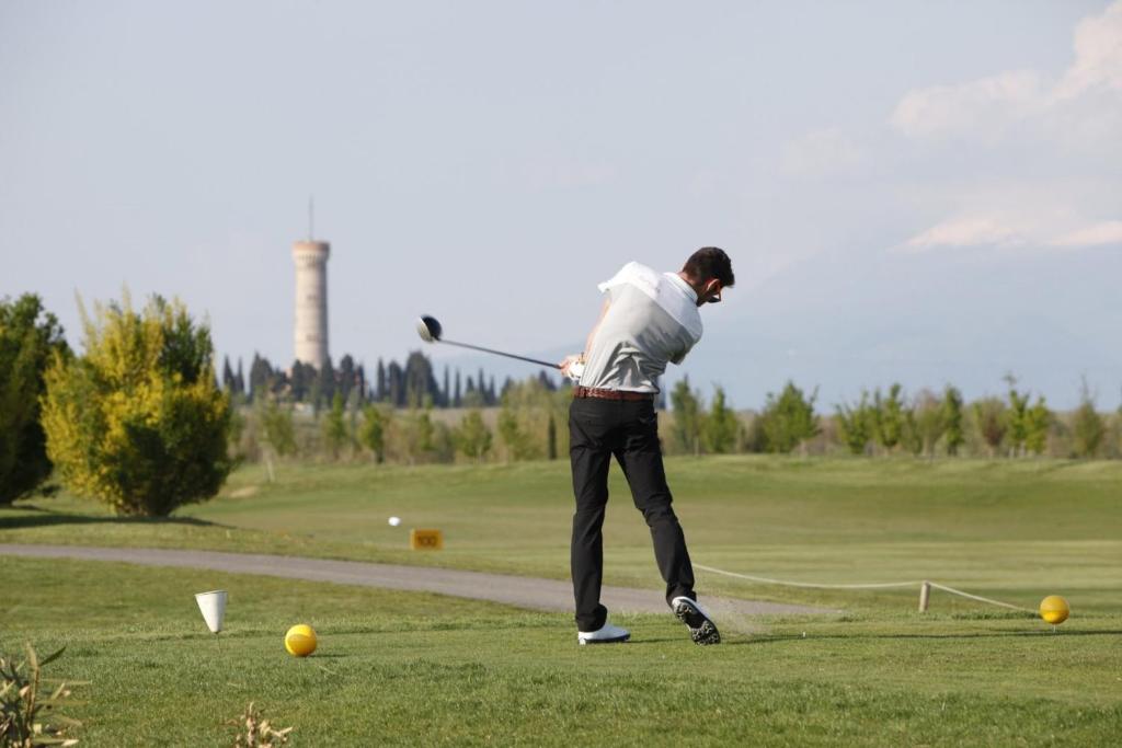 mężczyzna huśtający kijem golfowym na polu golfowym w obiekcie Garda Residence San Vigilio Golf w mieście Pozzolengo