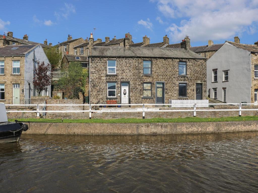 a house on the side of a river with buildings at Canal View Cottage in Keighley