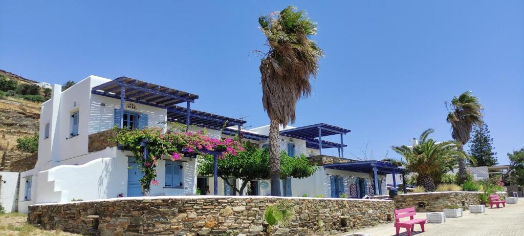 a white house with palm trees and a stone wall at Ethelio in Agios Ioannis Tinos