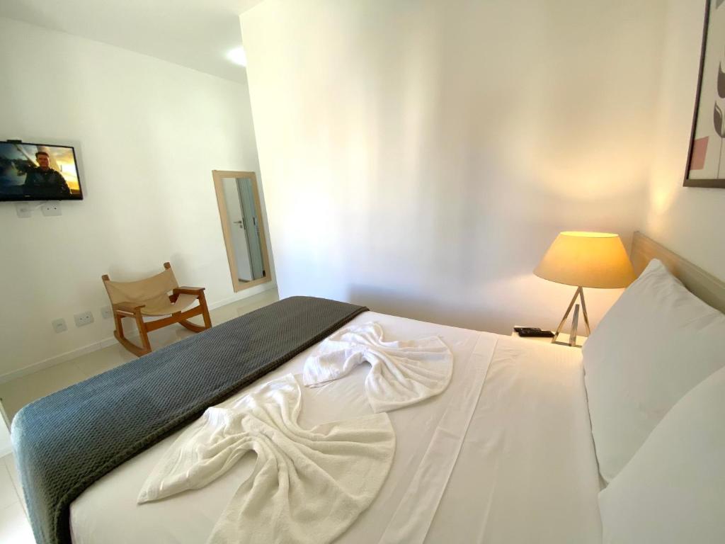 a bedroom with a white bed with a lamp and a chair at Apto Bella Citta em Cabo Frio in Cabo Frio