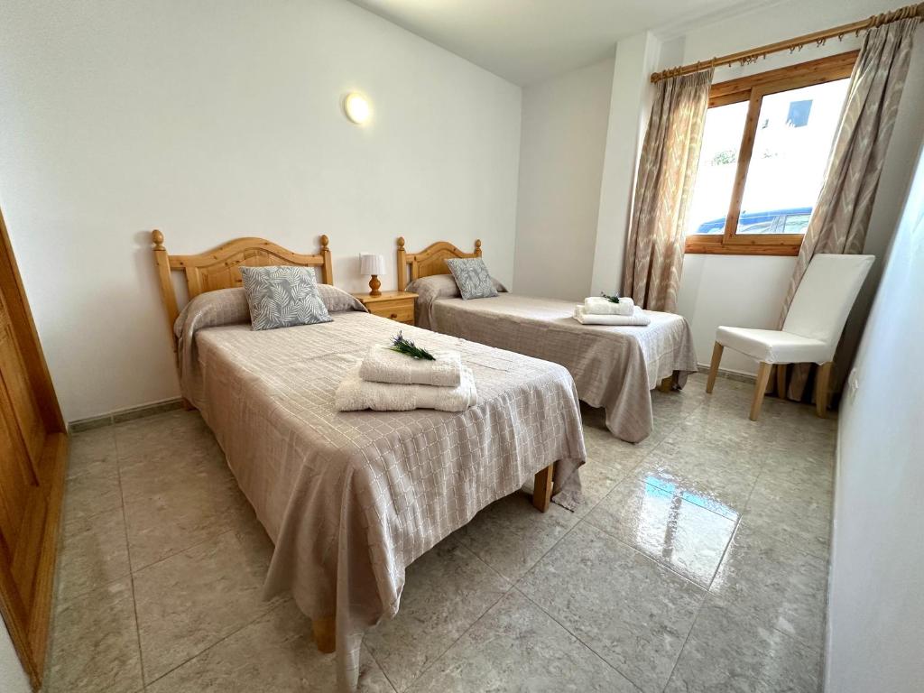 sypialnia z 2 łóżkami, krzesłem i oknem w obiekcie Apartamentos Sa Tenassa w miejscowości Colonia Sant Jordi
