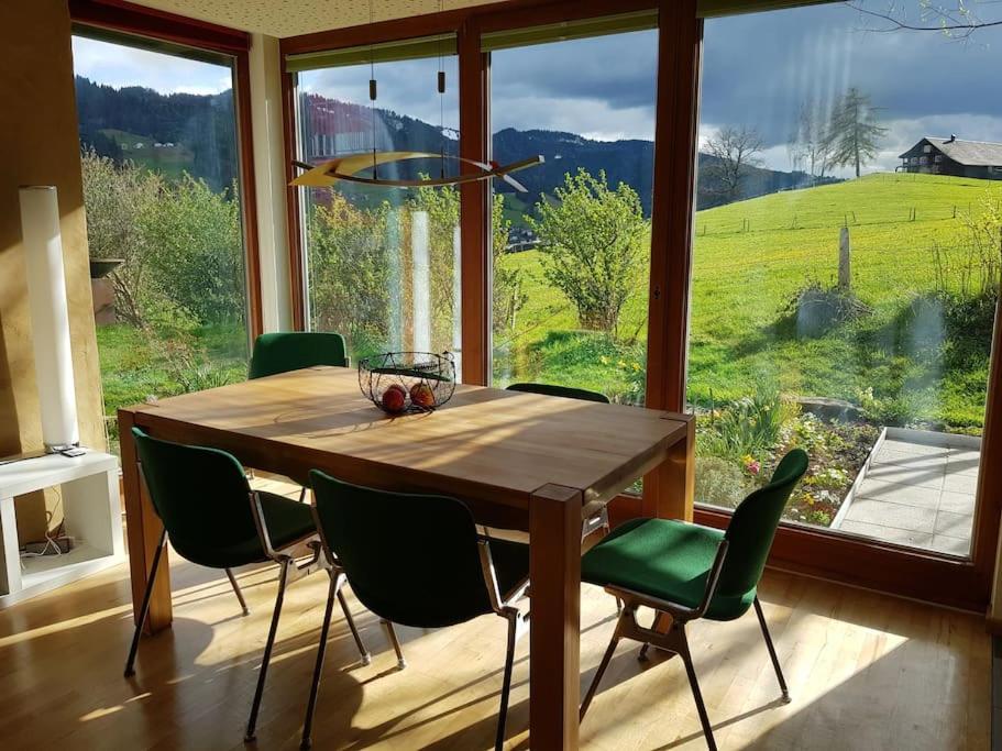 a dining room table with green chairs and a large window at Urlaub in Alberschwende in Alberschwende