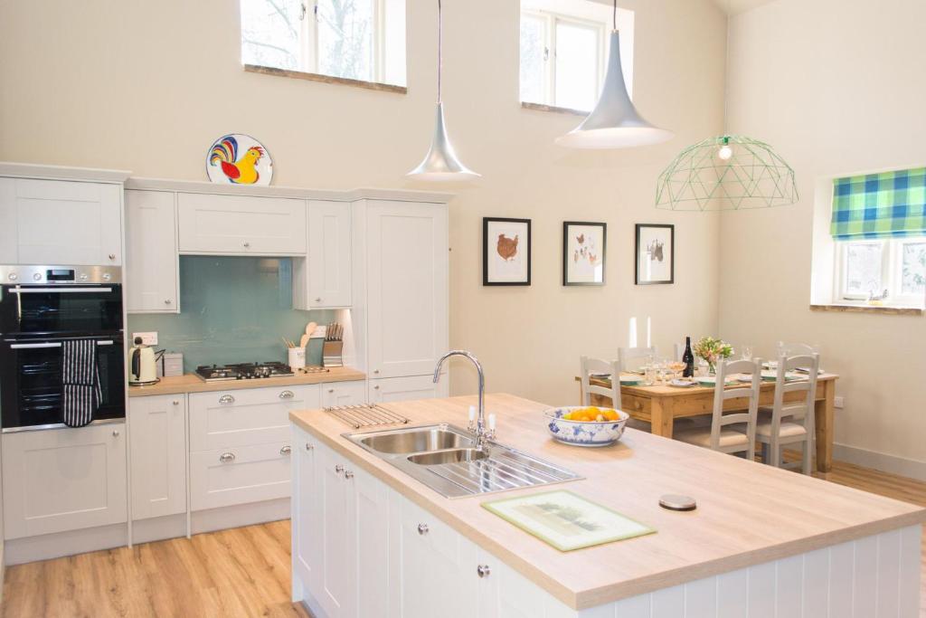 a kitchen with white cabinets and a sink and a table at Boathouse Barn in Coltishall