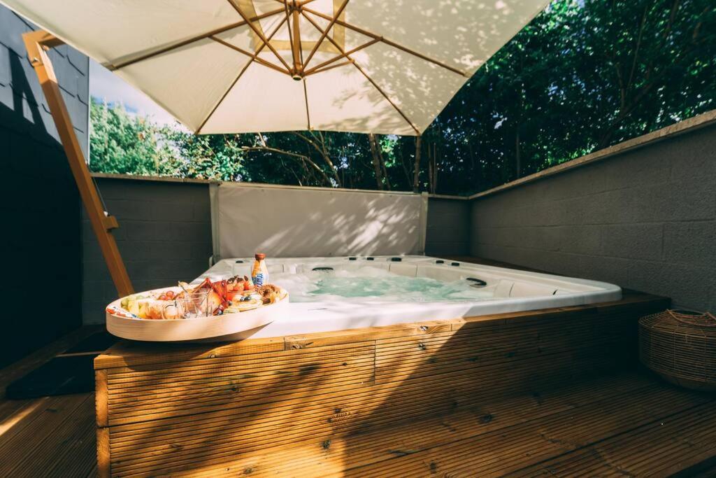 eine Whirlpool-Badewanne mit Sonnenschirm auf einer Holzterrasse in der Unterkunft Zenansa spa privatif in Quaregnon