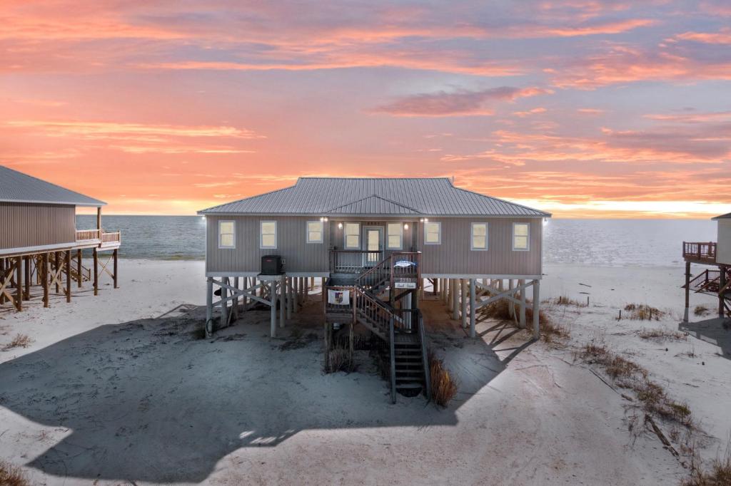 a house on the beach with a sunset in the background at Almost Heaven in Dauphin Island