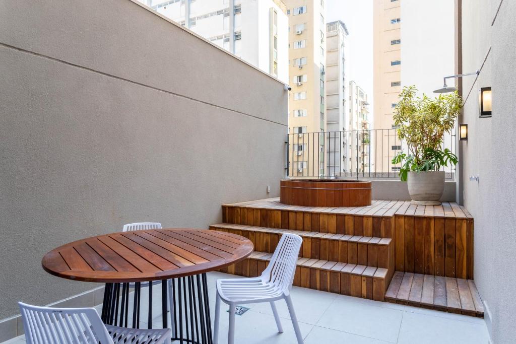 einen Balkon mit einem Holztisch, Stühlen und Treppen in der Unterkunft Apartamentos completos com academia ao lado da Av Paulista - Next Paulista in São Paulo