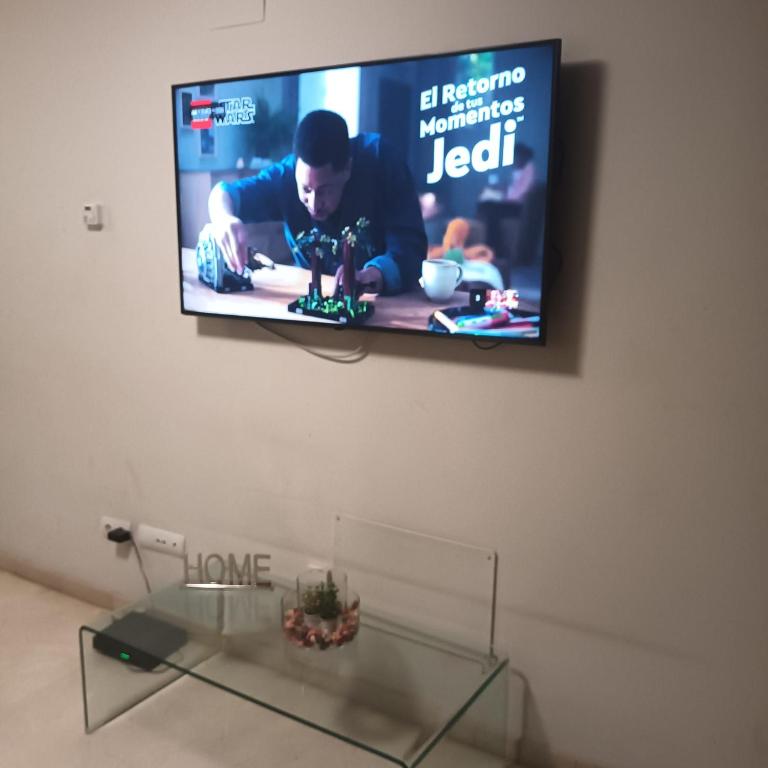una televisione appesa a un muro con un tavolo di vetro di Bcn apartments a Hospitalet de Llobregat