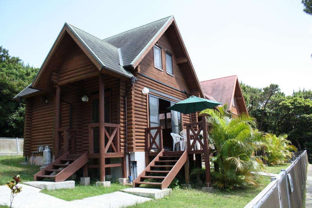 ein Blockhaus mit einer Veranda und einem grünen Sonnenschirm in der Unterkunft Tokashiki Guest House in Tokashiki