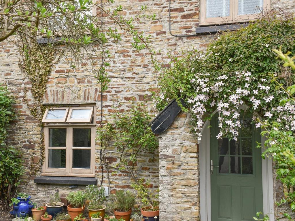 a brick building with a green door and flowers at Rose Cottage in Abbotsham