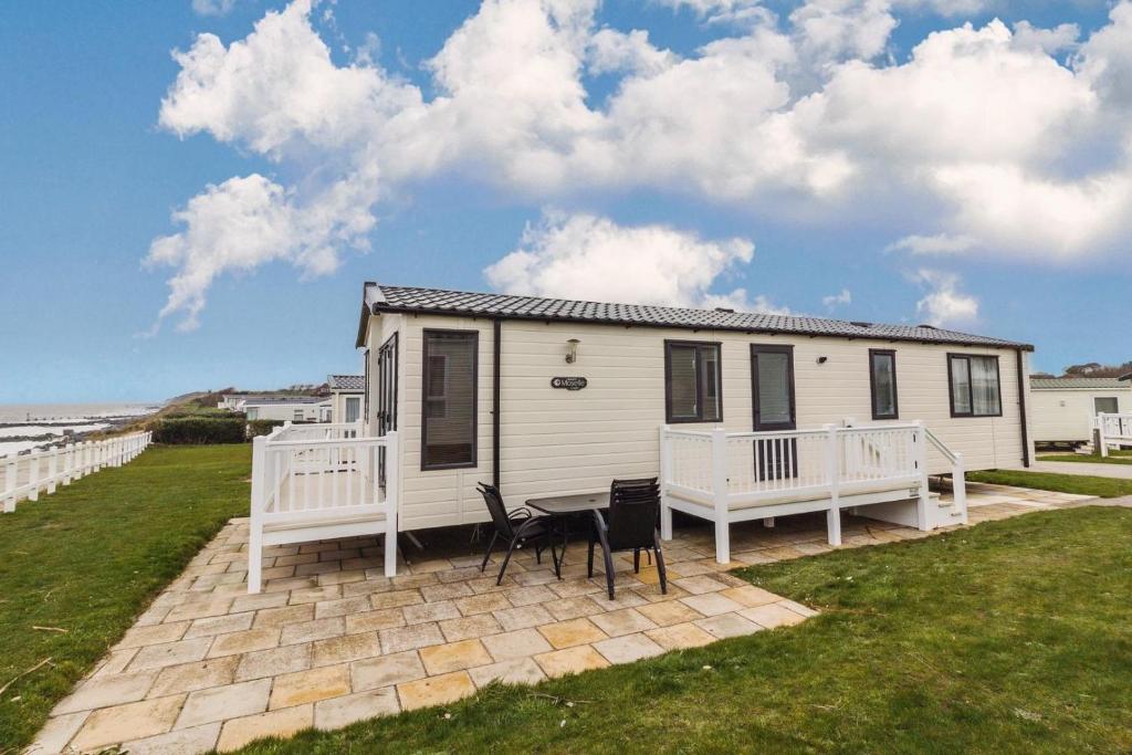 a small white house with two chairs on a patio at Luxury Caravan Boasting Full Sea Views At Hopton Holiday Park Ref 80041s in Great Yarmouth