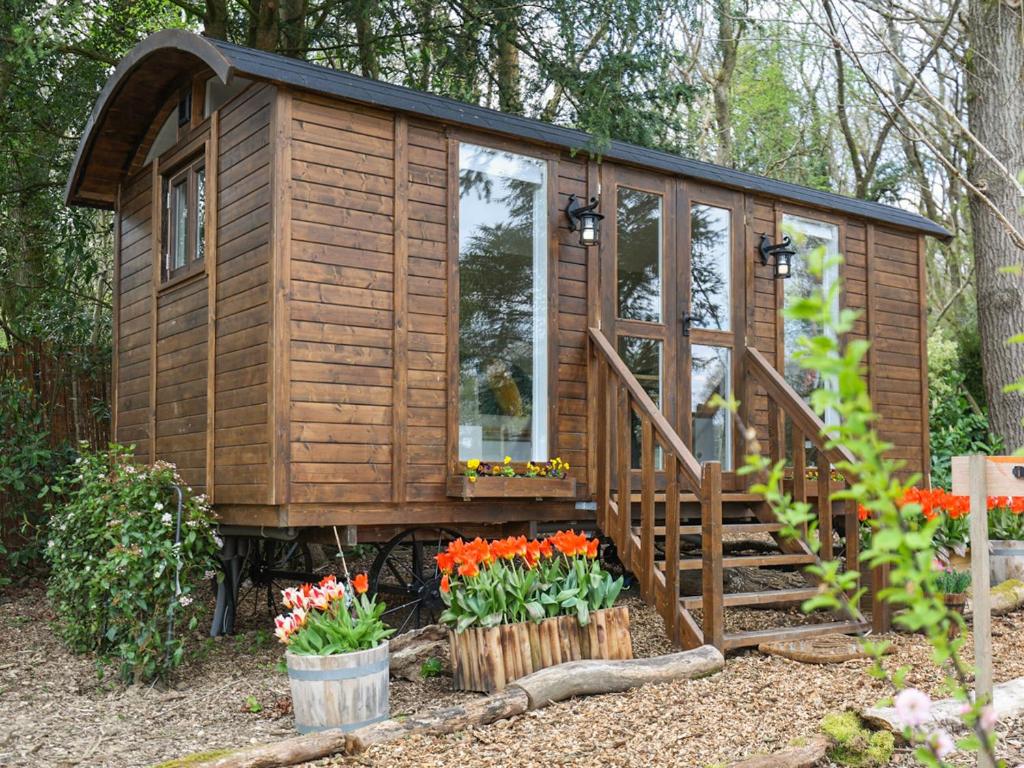 a wooden cabin in the woods with flowers at Sybs Farm Shepherds Hut in Fernhurst