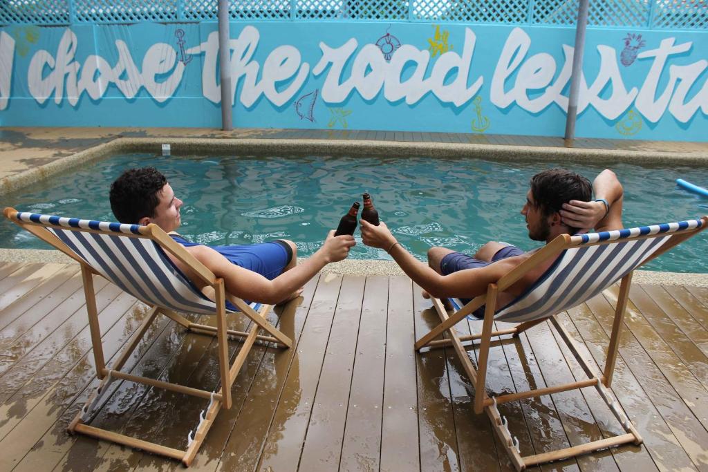 dos hombres sentados en sillas frente a una piscina en Port Douglas Backpackers en Port Douglas