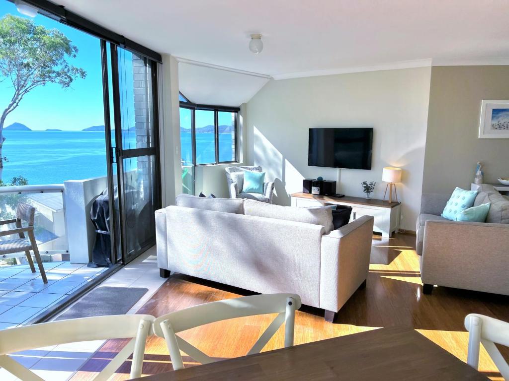 una sala de estar con muebles blancos y vistas al océano. en Tranquil Escape - Koala Hotspot - 2 Bed 2 Bath Apt Spectacular Sea Views en Soldiers Point