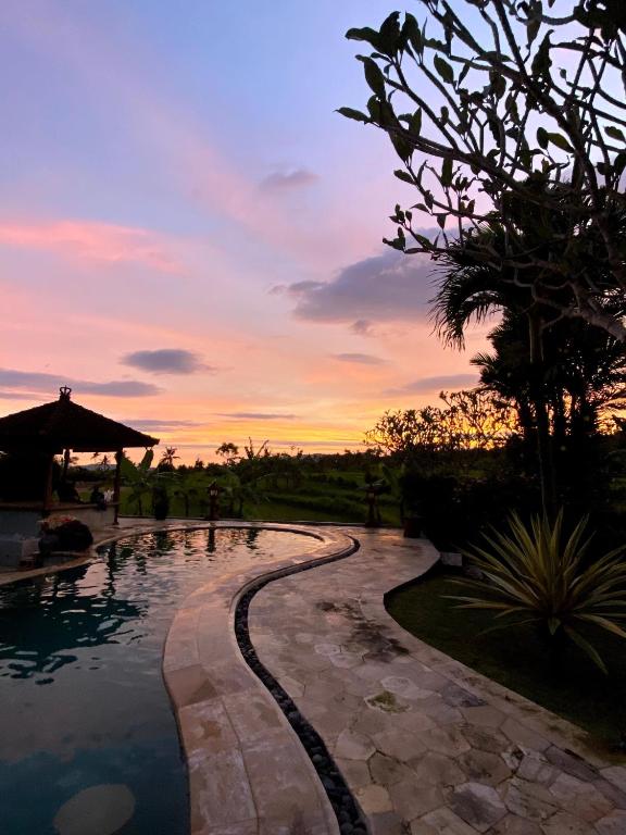 a resort swimming pool with a sunset in the background at Cabé Bali in Jasri