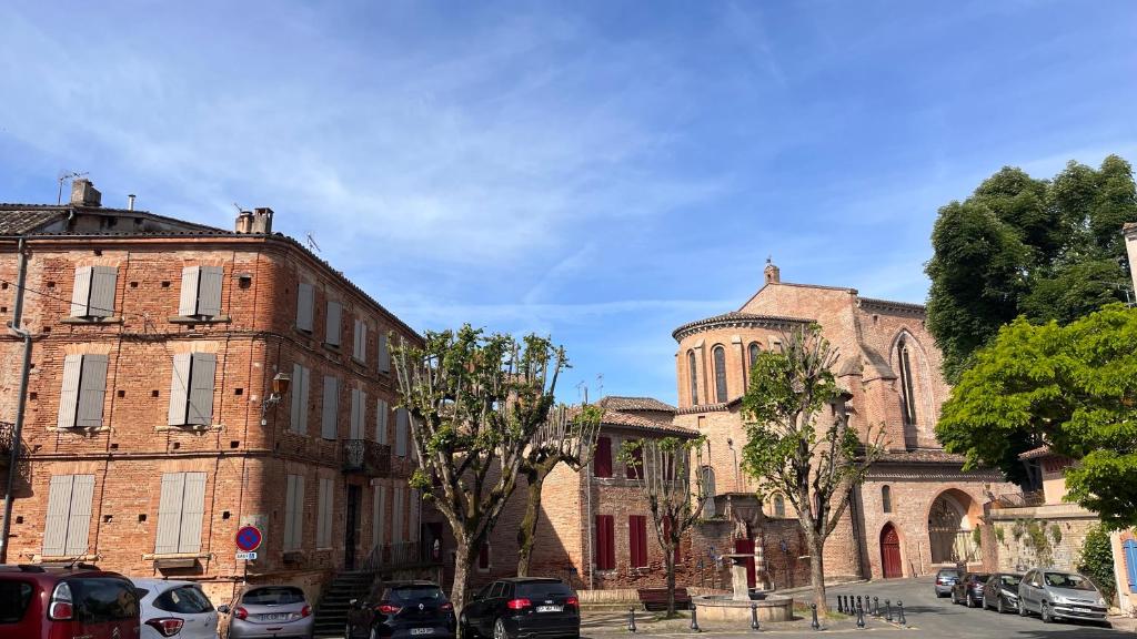 un gran edificio de ladrillo con coches estacionados frente a él en Le Gite d Eugenie en Gaillac