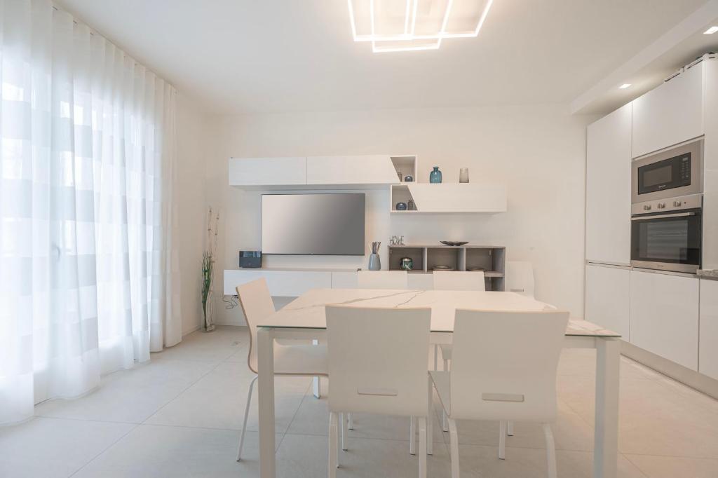 a white kitchen with a table and white chairs at Residence Luxury Elisabeth in Caorle