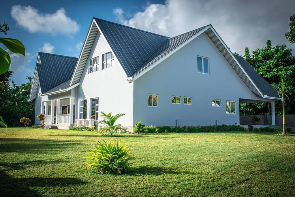 a white house with a black roof and a yard at Island Charm of Praslin in Victoria