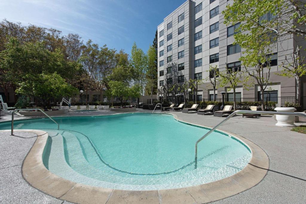 une grande piscine avec des chaises et un bâtiment dans l'établissement Hyatt Centric Santa Clara Silicon Valley, à Santa Clara