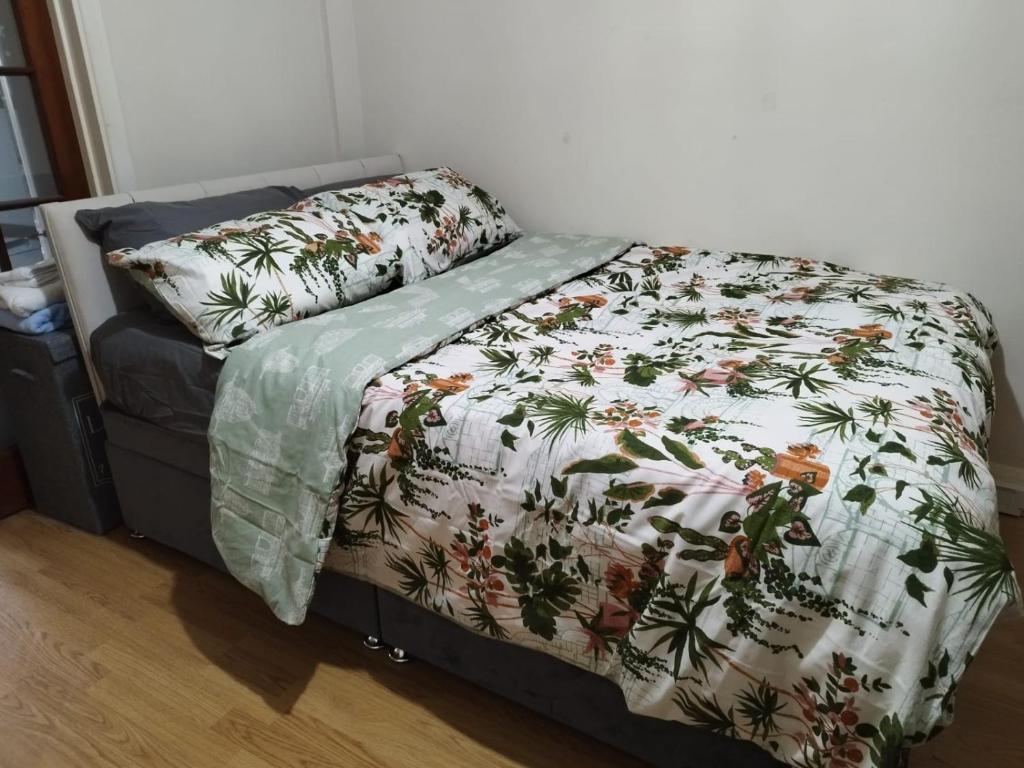 a bed with a flowered comforter and pillows on it at Nice Studio Flat in Edmonton, North London in Edmonton