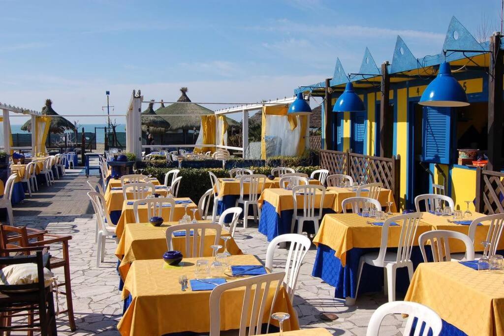 una fila de mesas y sillas con mesas amarillas y sillas blancas en Casa Levante Fregene, mare e relax vicino Roma, en Fregene