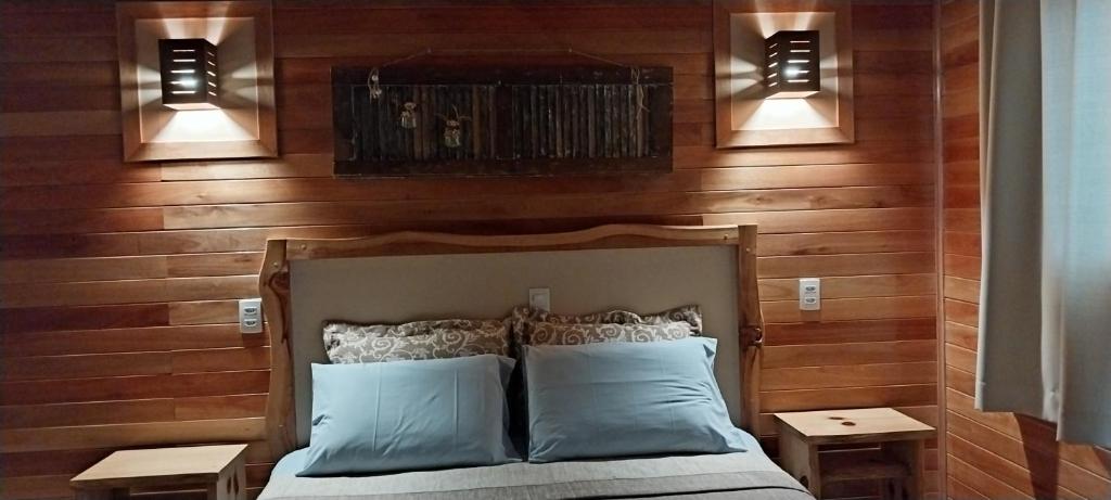 1 dormitorio con pared de madera, 1 cama y 2 luces en Pousada Sentiero, en Urubici