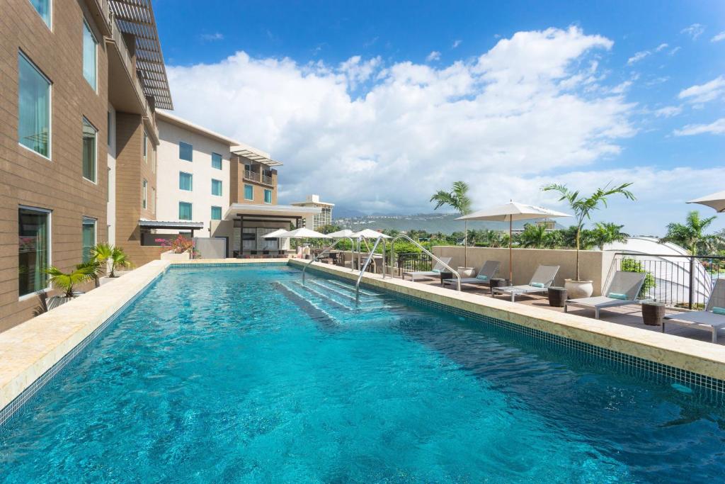 a pool with chairs and umbrellas next to a building at Courtyard by Marriott Kingston, Jamaica in Kingston