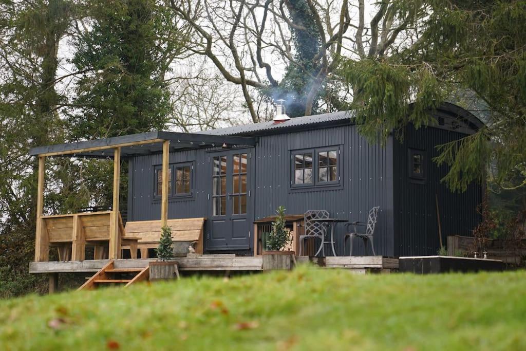 Shepherds Hut in countryside near Bath and Bristol في بريستول: منزل صغير زرقاء مع شرفة على العشب