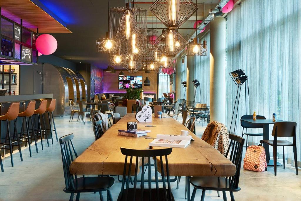 a restaurant with a large wooden table and chairs at Moxy Paris Charles de Gaulle Airport in Roissy-en-France